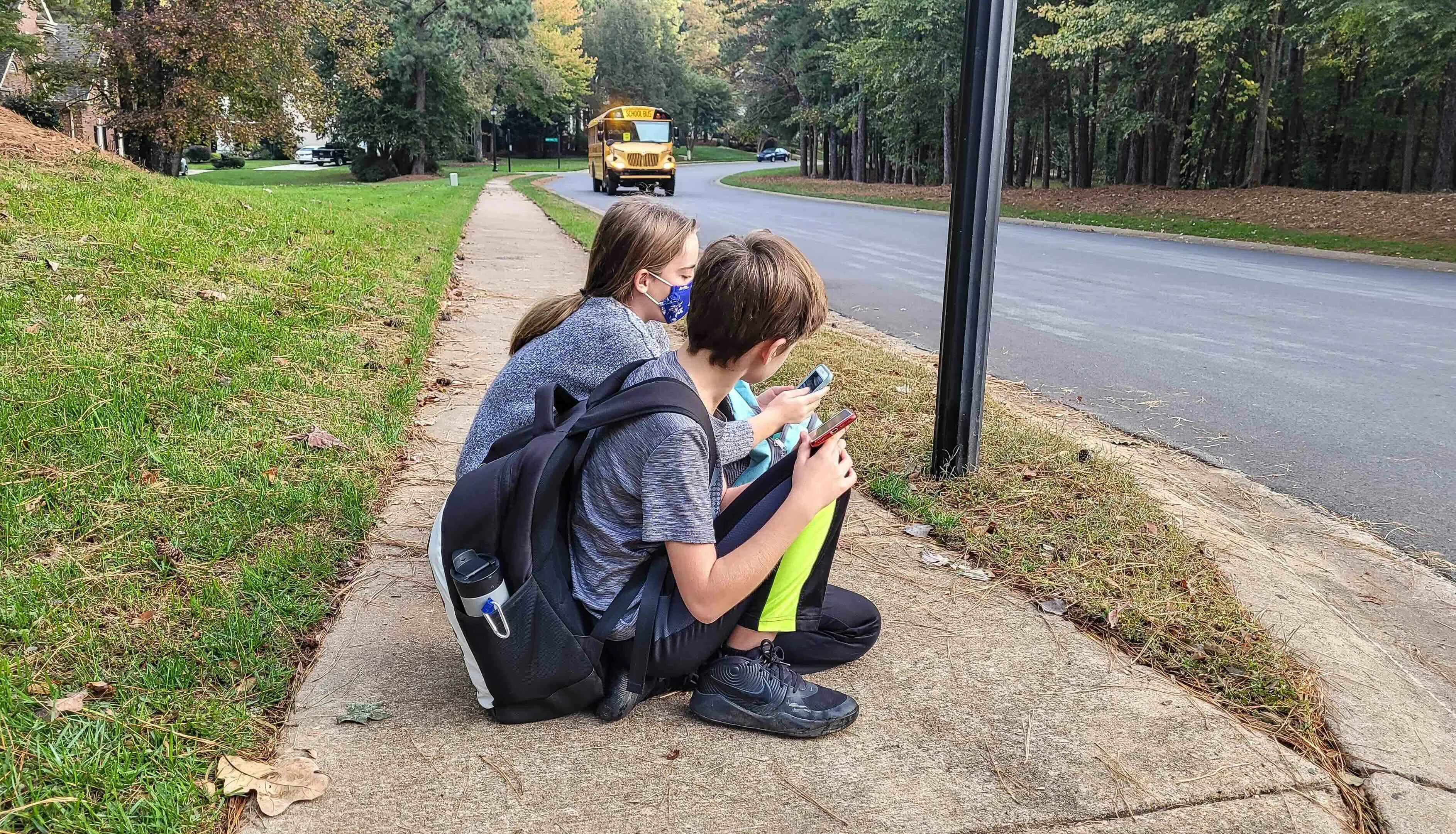 Dos hermanos esperando el microbús escolar en la acera